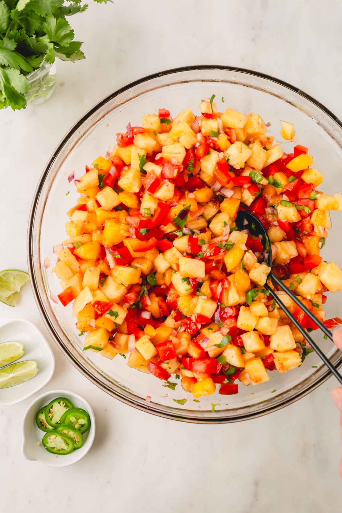 Pineapple mango salsa mixed in a large glass bowl with a black serving spoon.