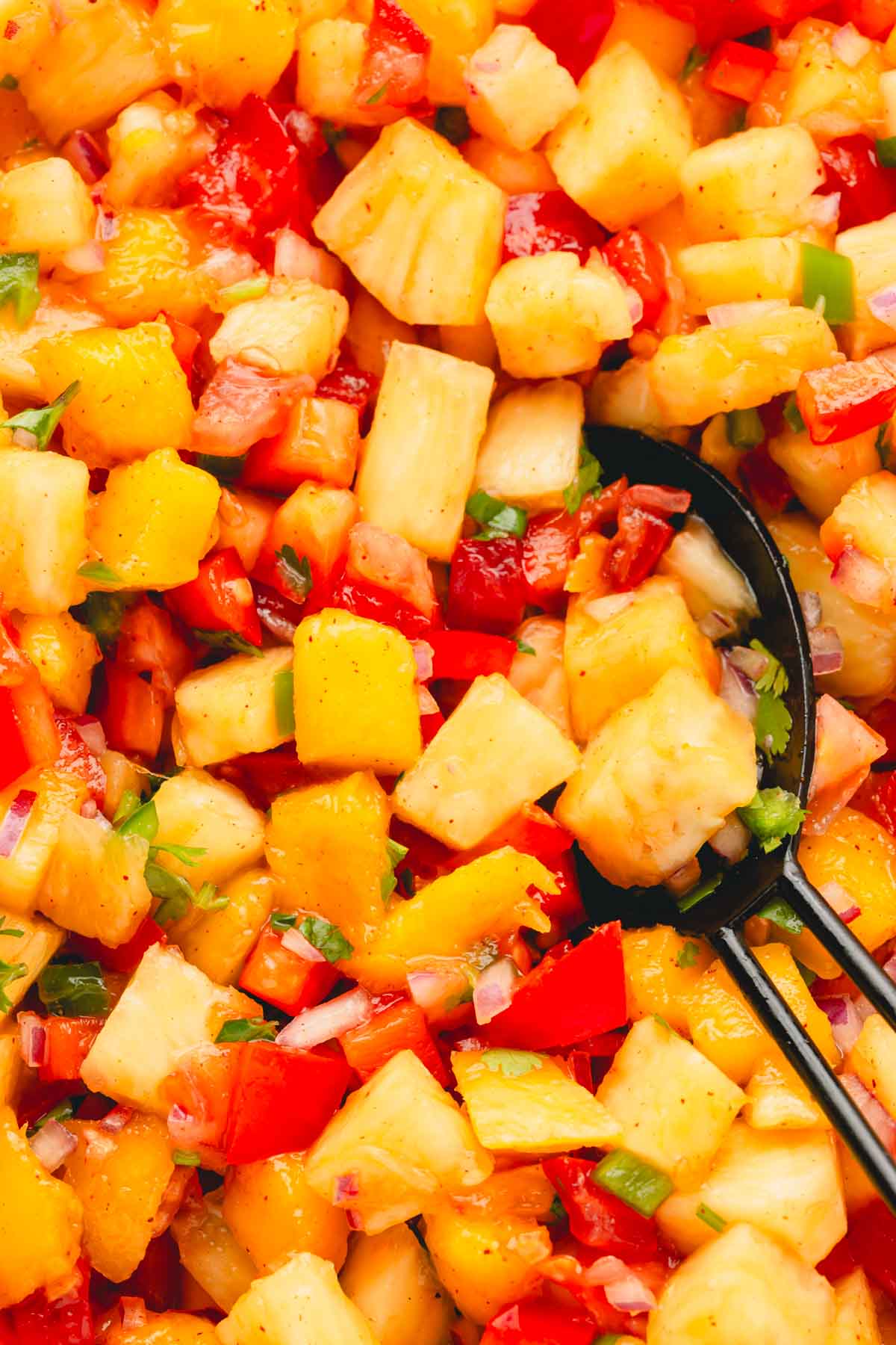 A closeup image of pineapple mango salsa with a black serving spoon.