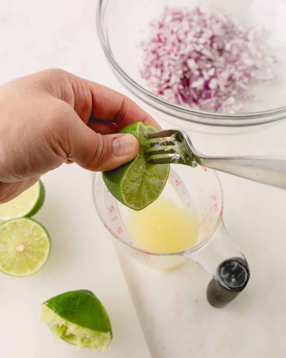 A hand is juicing a lime half with a fork.
