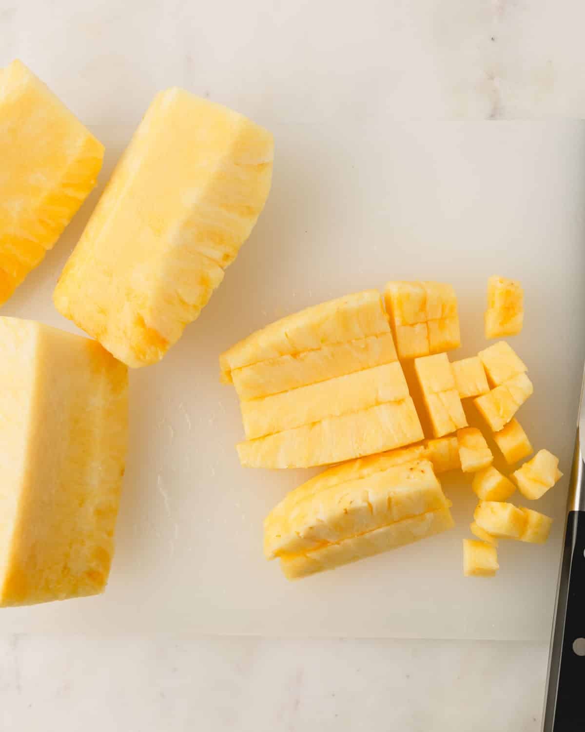 Pineapple is being cubed on a cutting board.