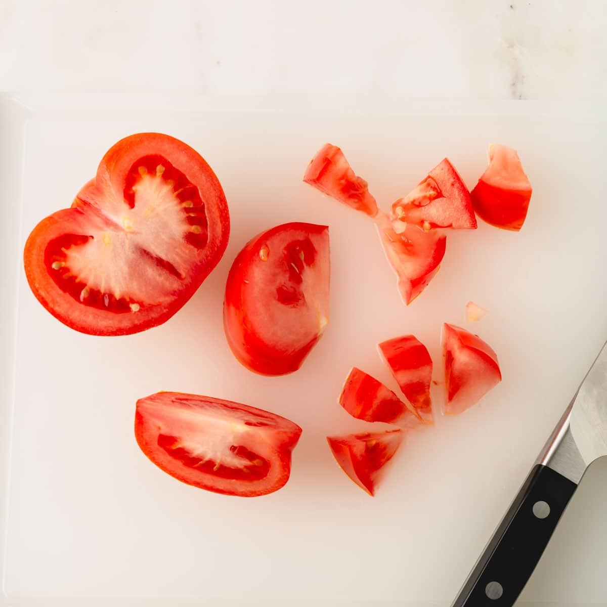 Tomatoes being chopped on a cutting board with a knife.