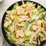 Caesar pasta salad in a black bowl with a large spoon.