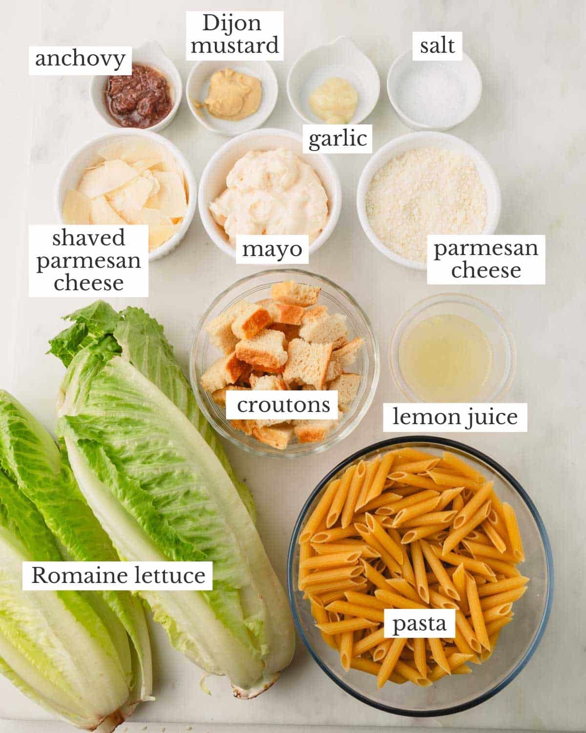 Ingredients for Caesar pasta salad which include anchovy, Dijon mustard, garlic, salt, parmesan cheese, mayonnaise, croutons, lemon juice, romaine, and pasta.