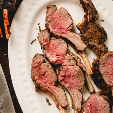 Grilled rack of lamb is cut into lamb chops on a white serving platter.