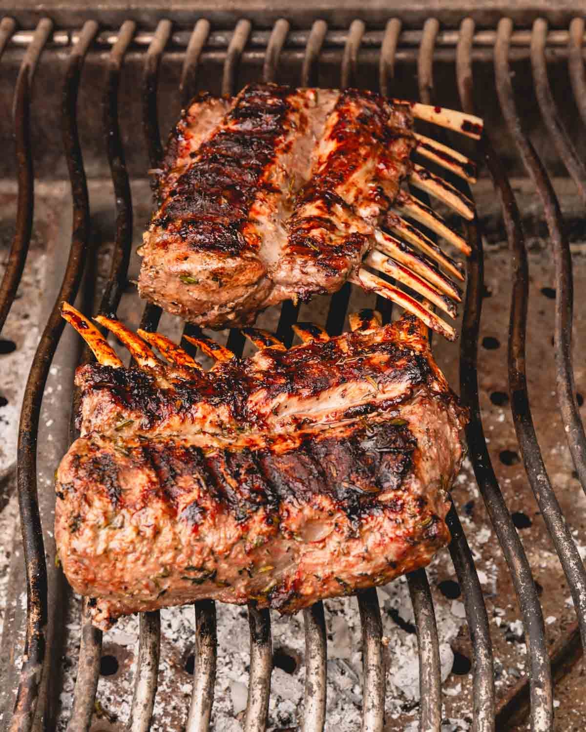 Two racks of lamb are grilling over indirect heat bone side down.