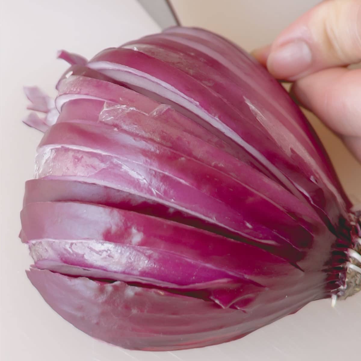Half of red onion cut side down and being sliced.