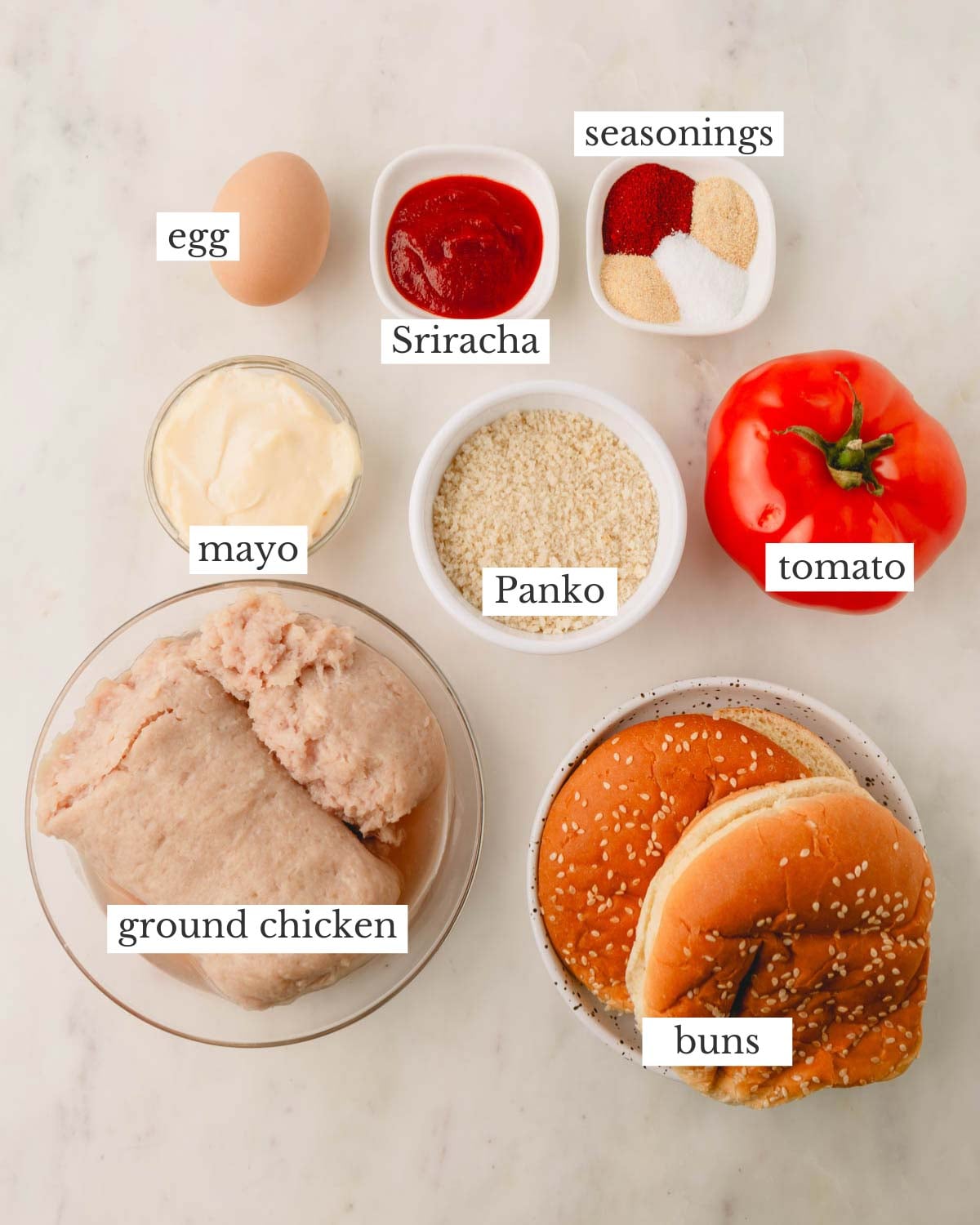 Ingredients for spicy chicken burgers which include egg, mayonnaise, sriracha, panko, ground chicken, tomato, buns, and seasonings.