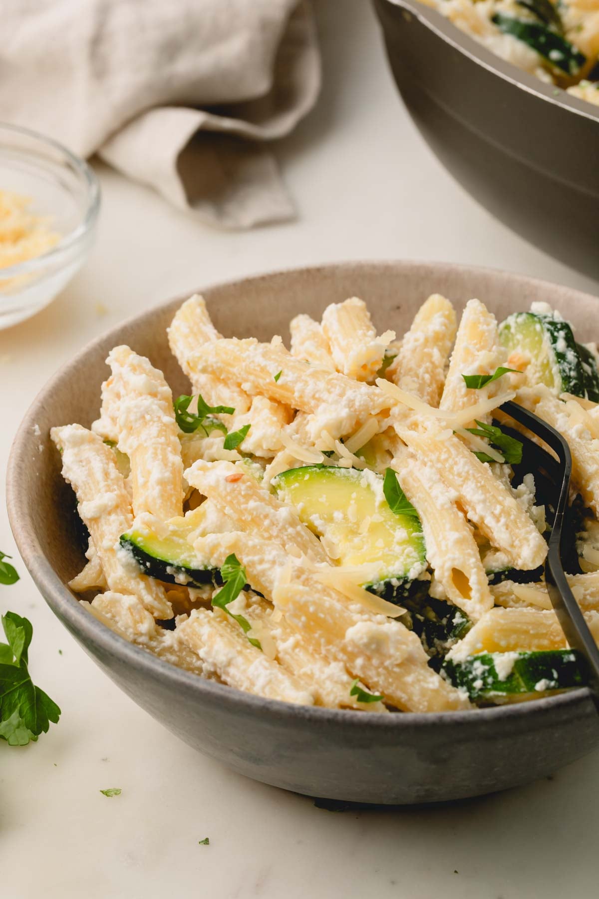 A close up image of zucchini ricotta pasta in a brown bowl with a fork.