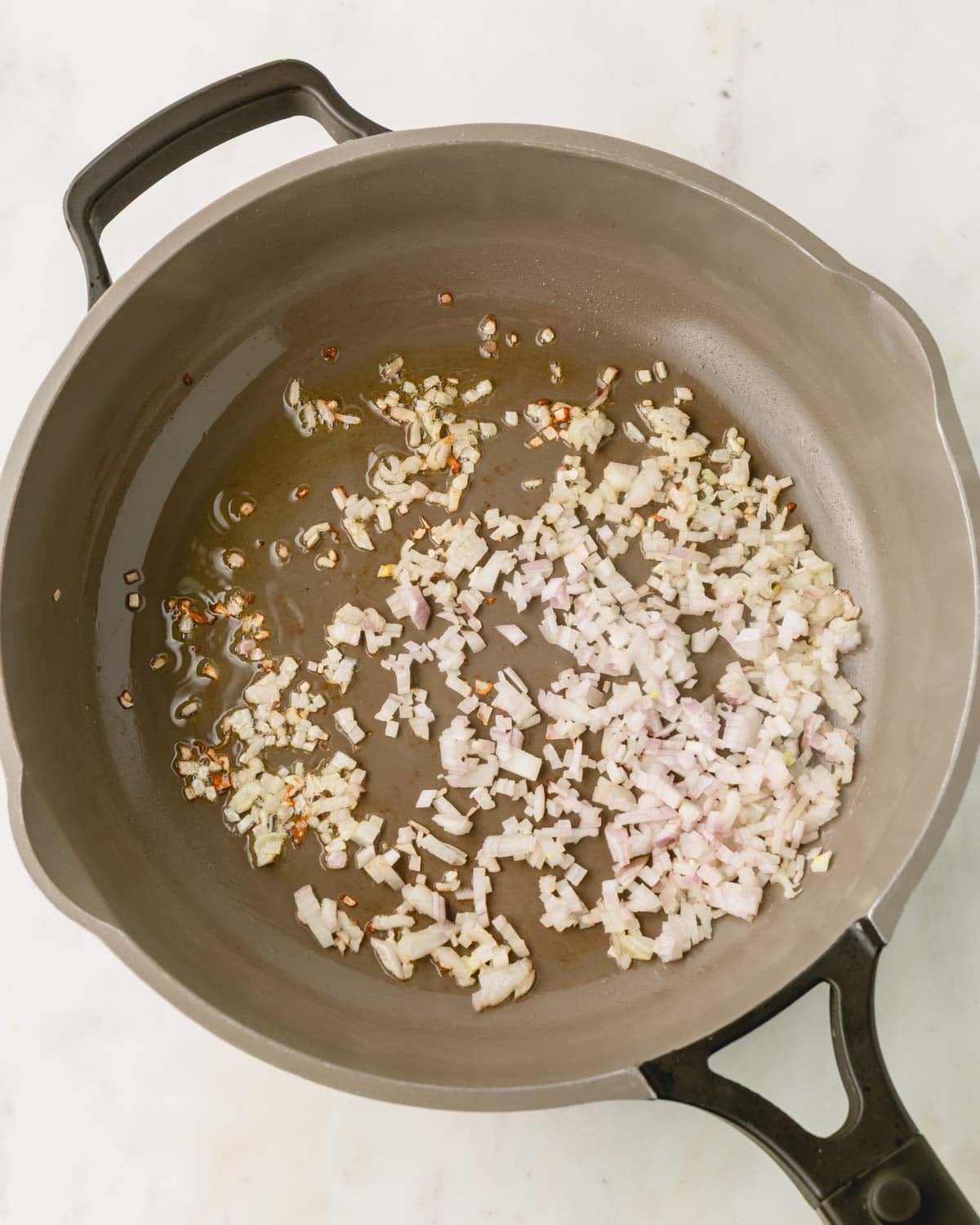 A large skillet is cooking shallot in olive oil.