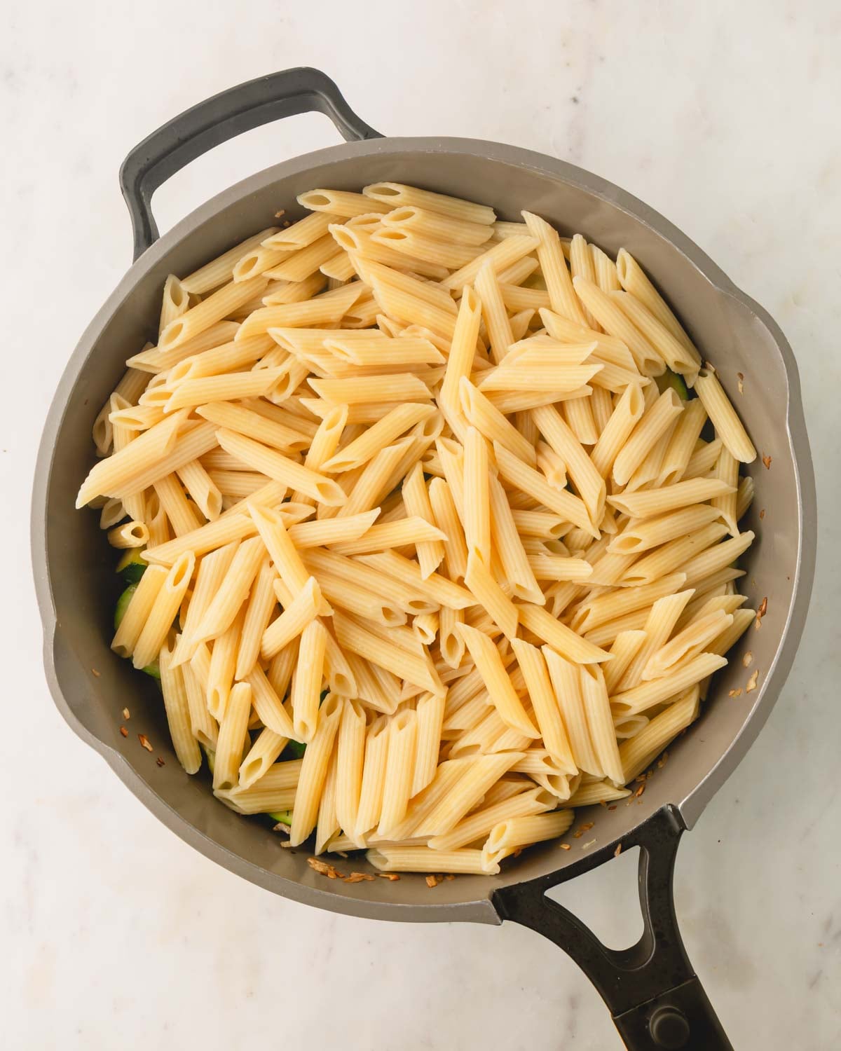 Cooked penne pasta is added to the large skillet.