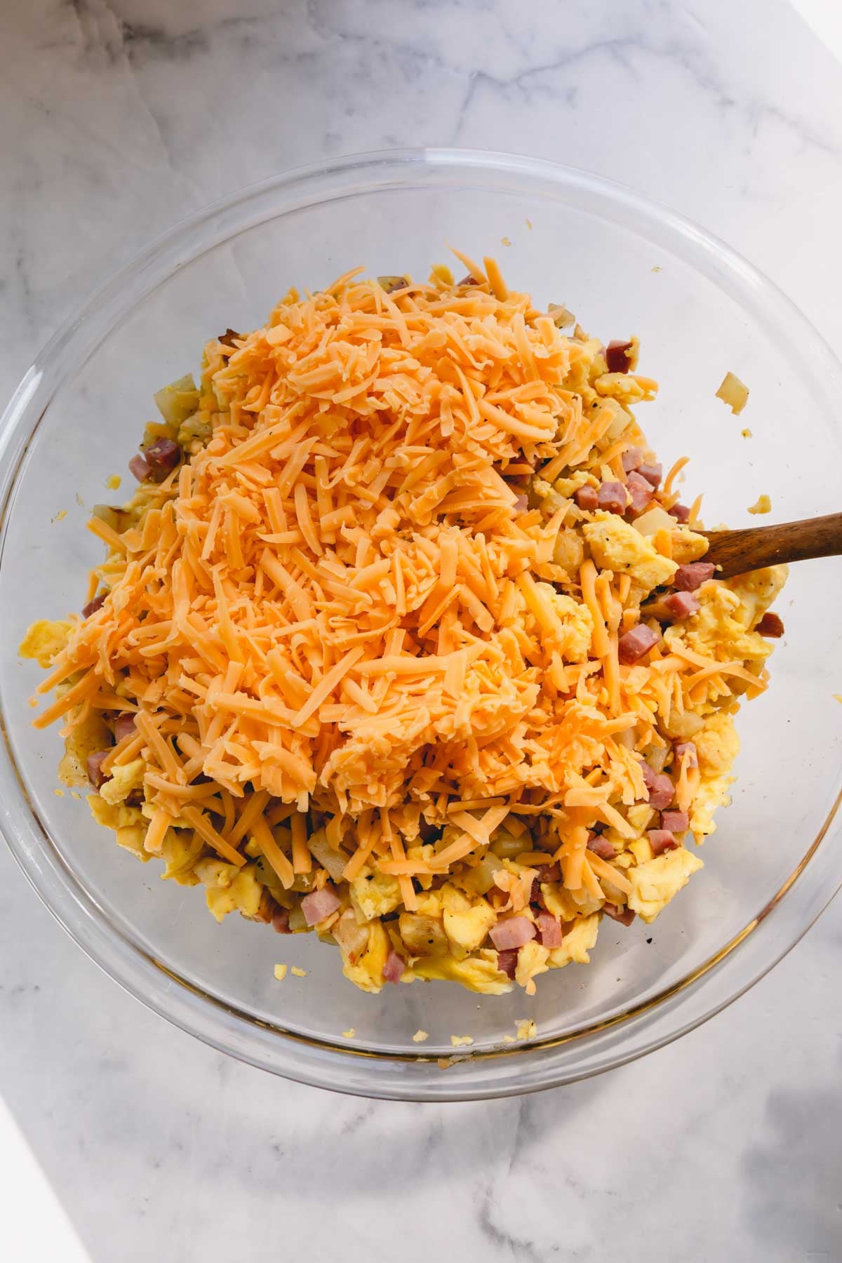 Shredded cheddar cheese on top of scrambled eggs and cubed ham.