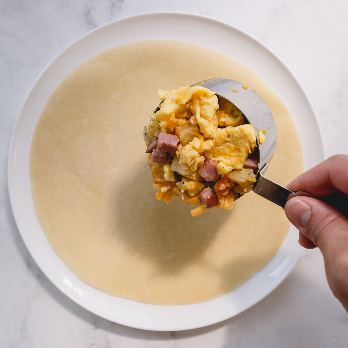Burrito filling scooped into a dry measuring cup over a tortilla wrap on a white plate.