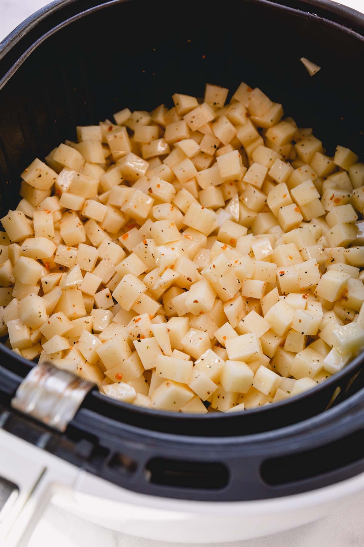 Cubed and seasoned potatoes in a airfryer basket.