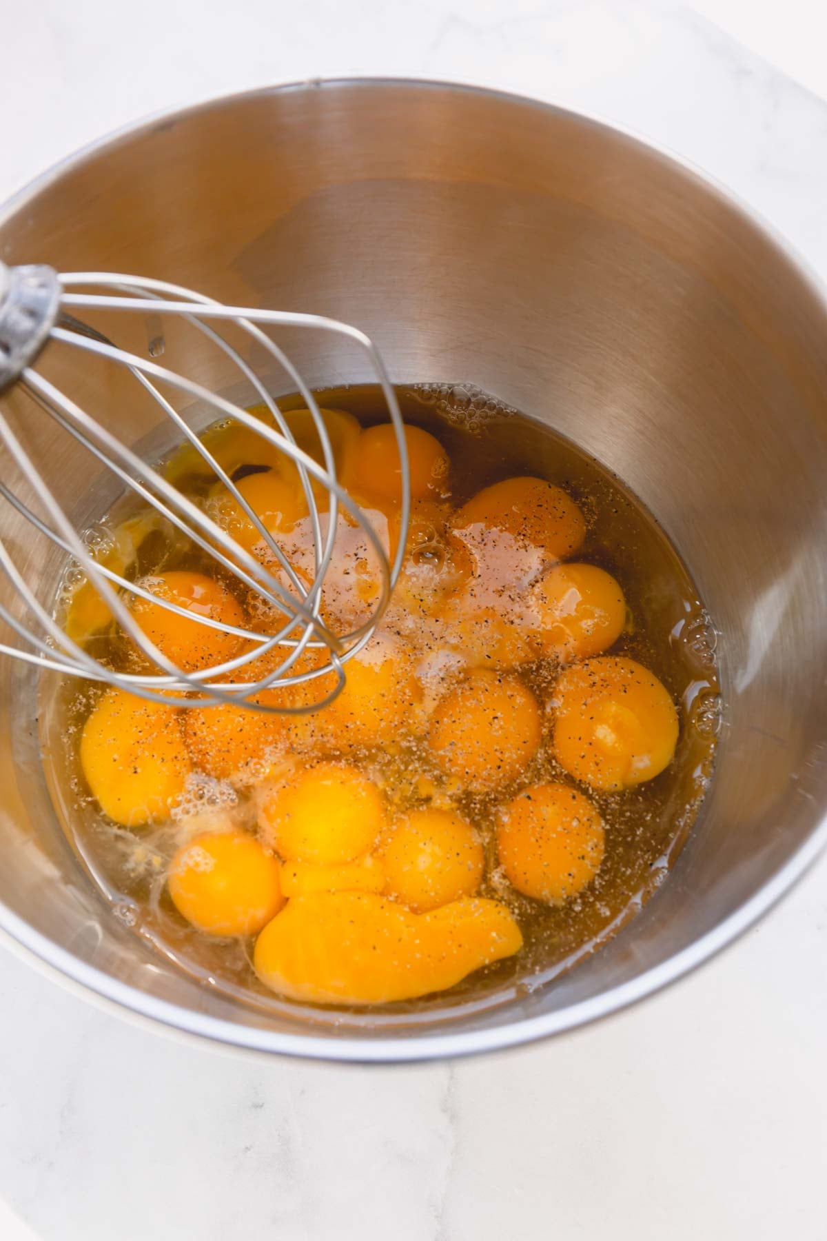Dozen raw eggs cracked in a stand mixer bowl with a whisk attachment.