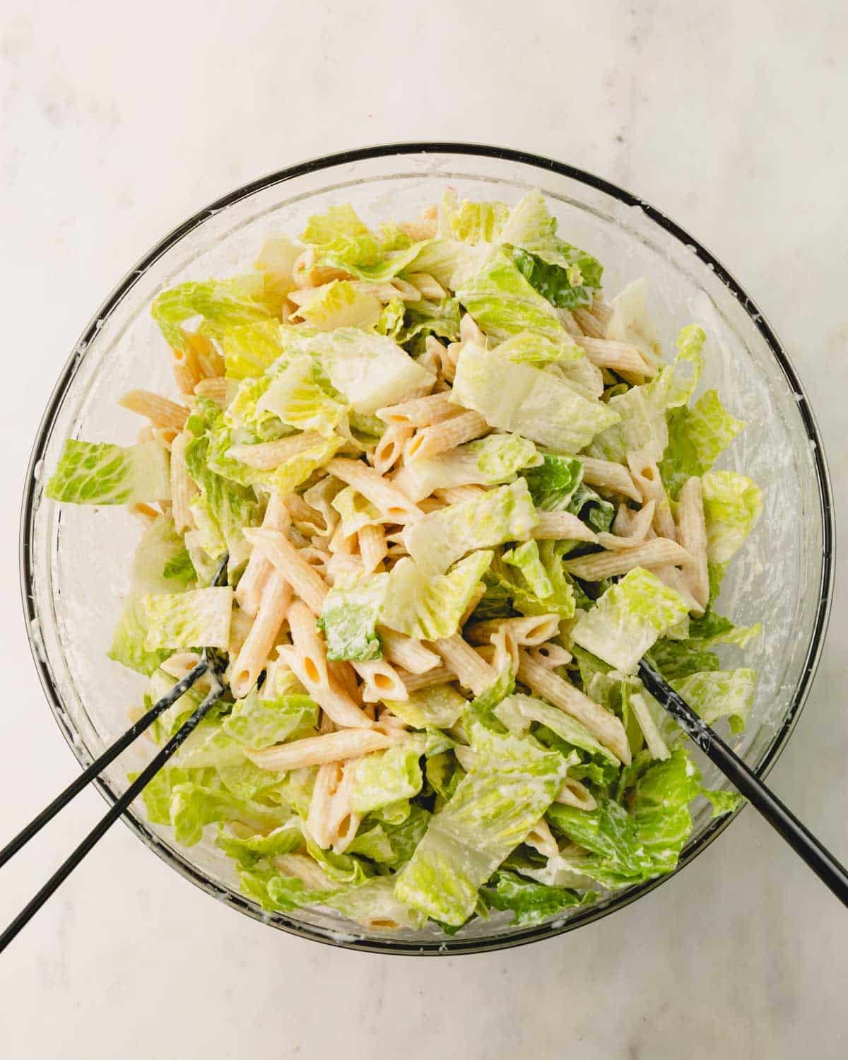 Caesar pasta salad mixed in a large glass bowl.