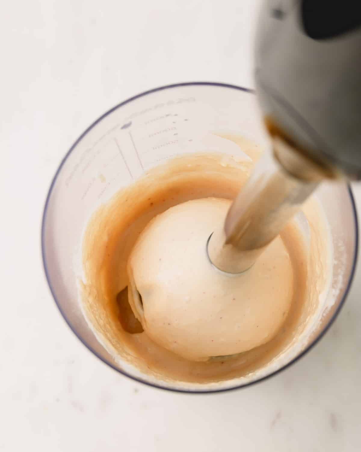 Caesar dressing ingredients in a blender cup with an immersion blender mixing the ingredients.