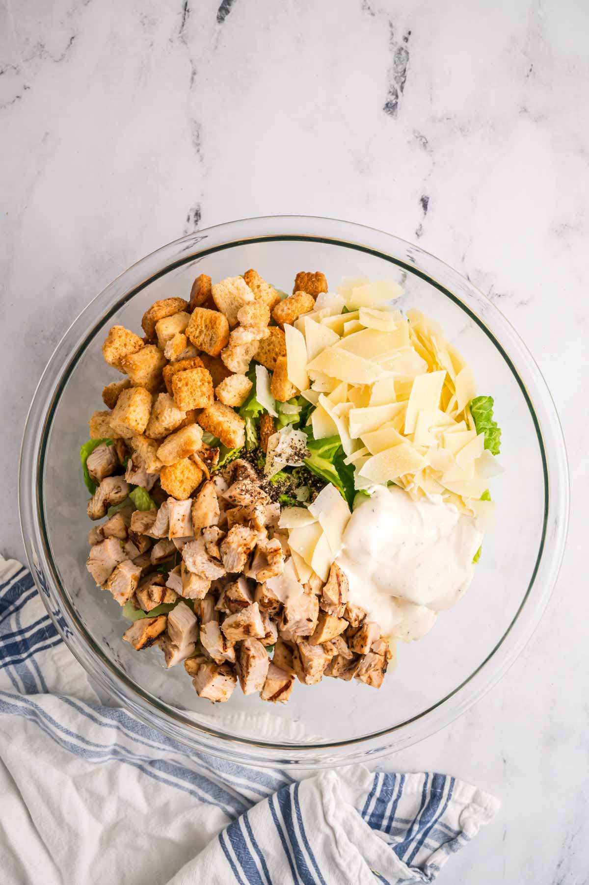 A glass bowl with caesar salad ingredients in piles.