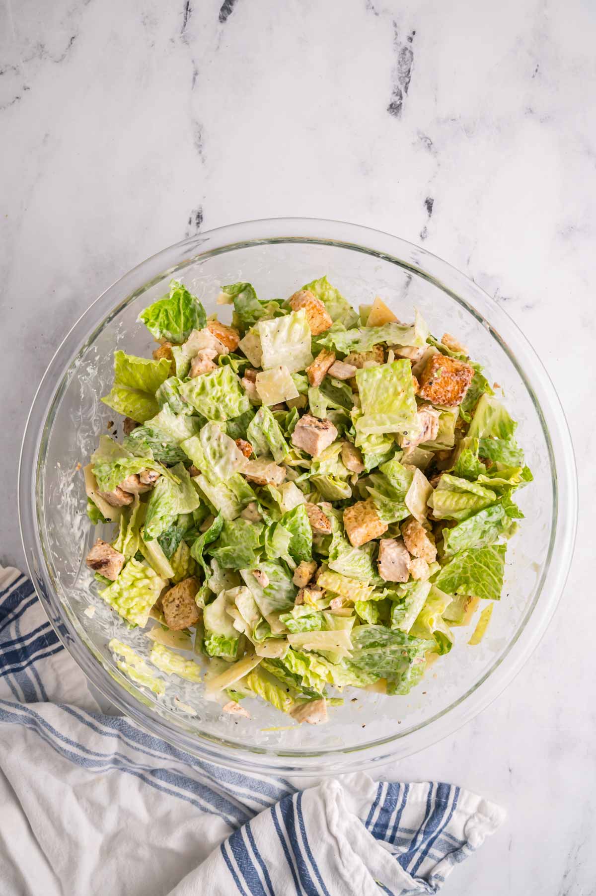 Chicken caesar salad is mixed in a glass bowl.