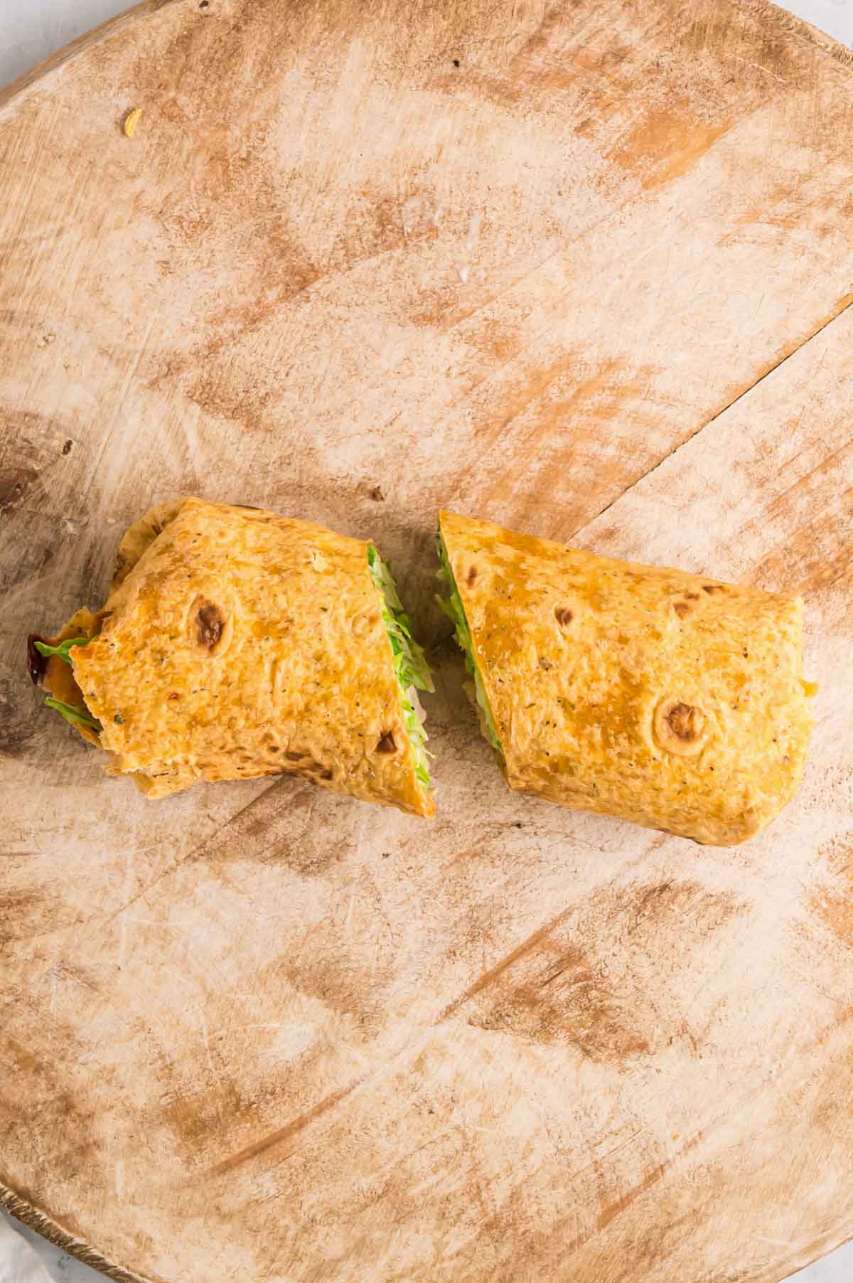 Chicken caesar salad wrap is rolled and cut on a wooden cutting board.
