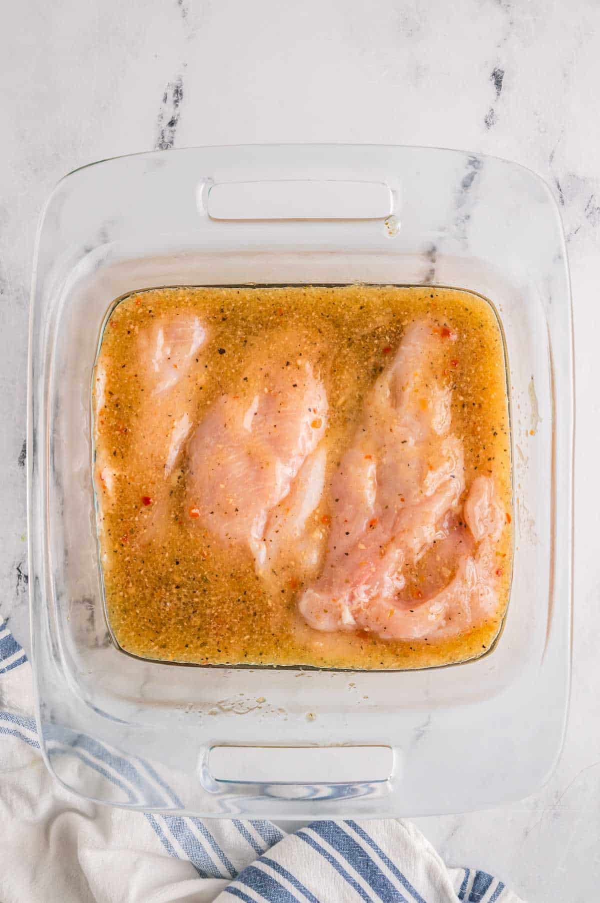 Chicken breasts marinating in Italian dressing in a glass baking dish.