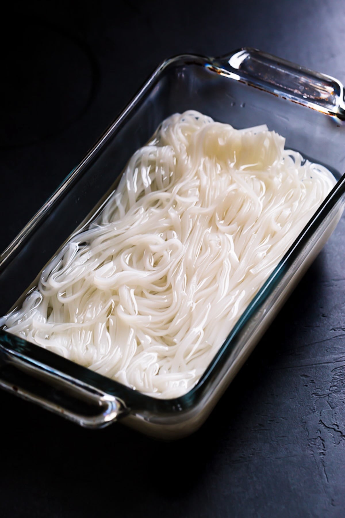 Rice noodles are soaking in a baking dish with water.