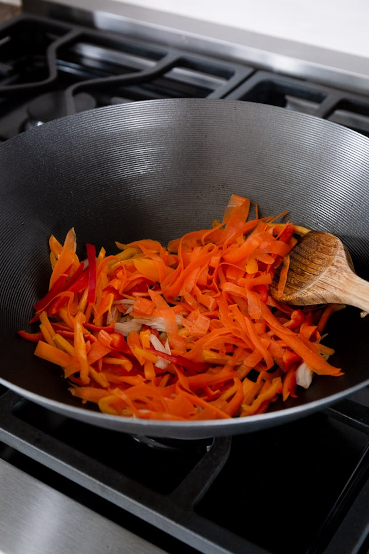 A wok is cooking vegetables with a wooden spoon.