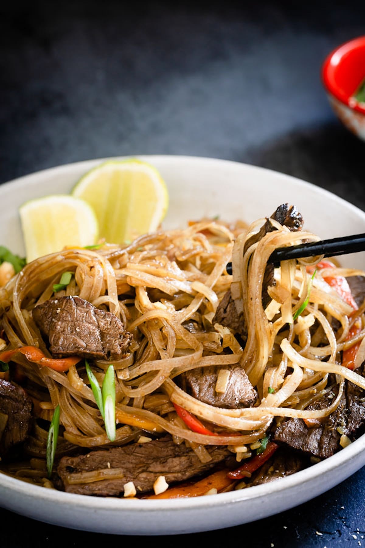 Chopsticks are holding up beef pad thai in a gray bowl.