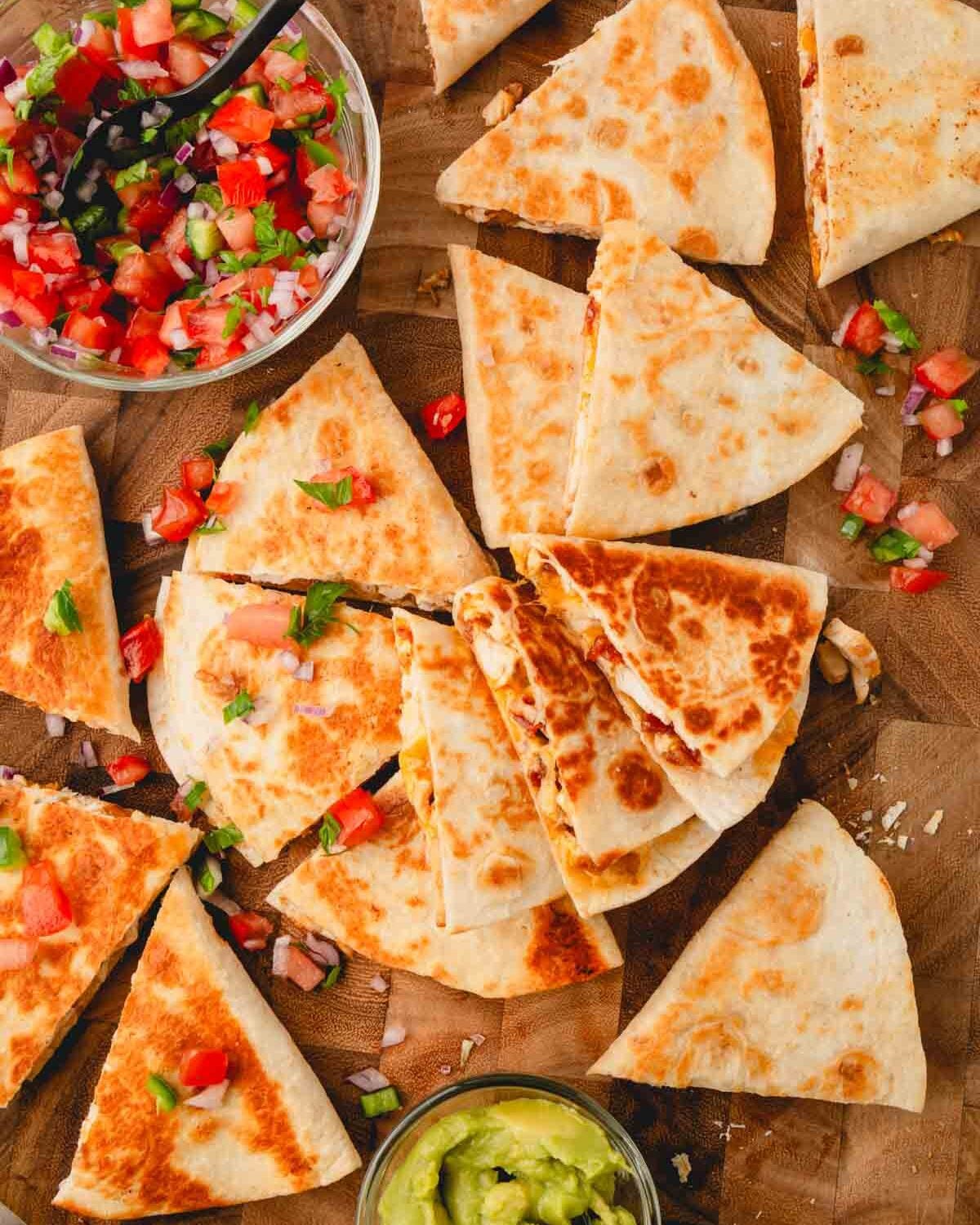 A wood cutting board with chicken bacon ranch quesadillas, pico de gallo, and guacamole.