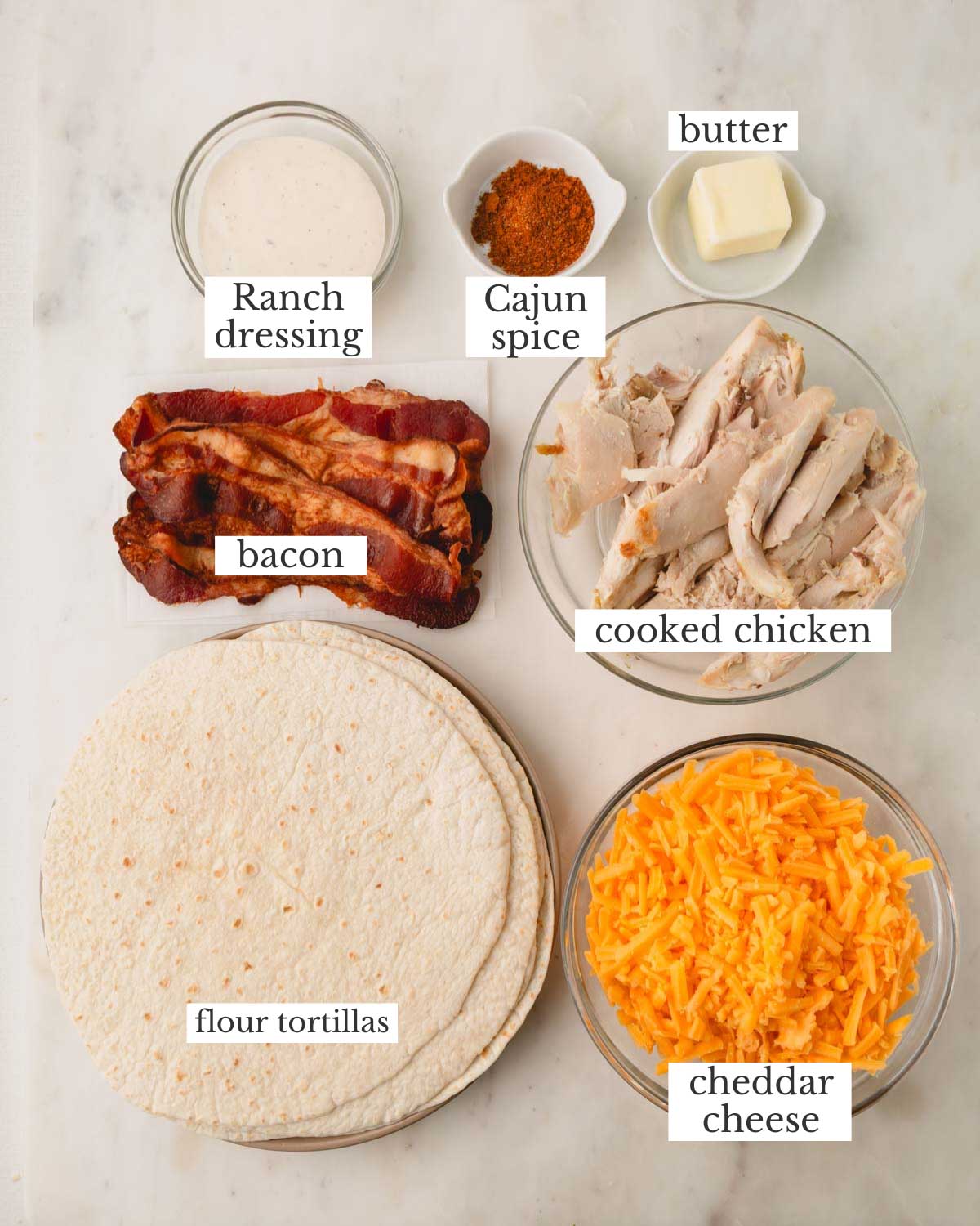 Ingredients for chicken bacon ranch quesadillas, which include chicken, cheddar cheese, butter, cajun spice, ranch dressing, bacon, flour tortillas.