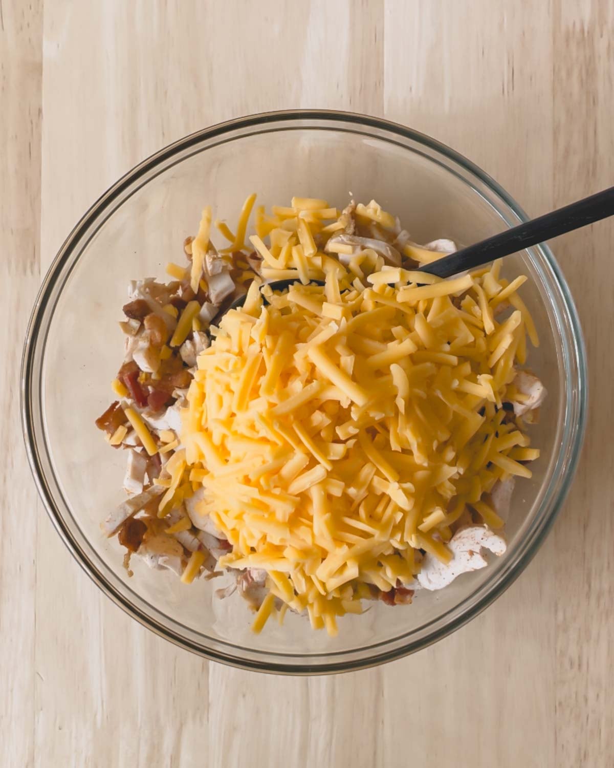 Shredded cheddar cheese is added to the glass bowl of the chicken bacon ranch filling.