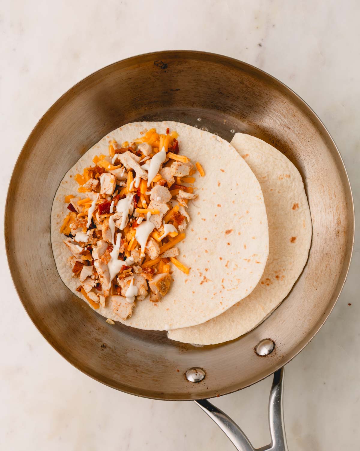 A skillet is cooking two chicken bacon ranch quesadillas.