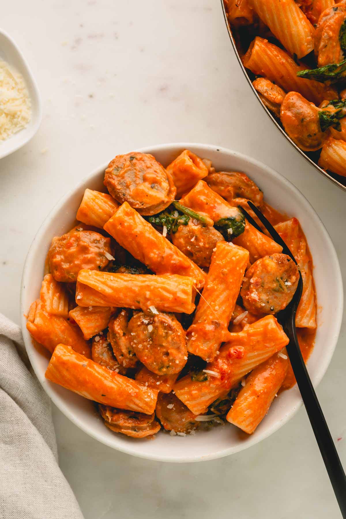 A white bowl of chicken sausage and pasta with a black fork in it.