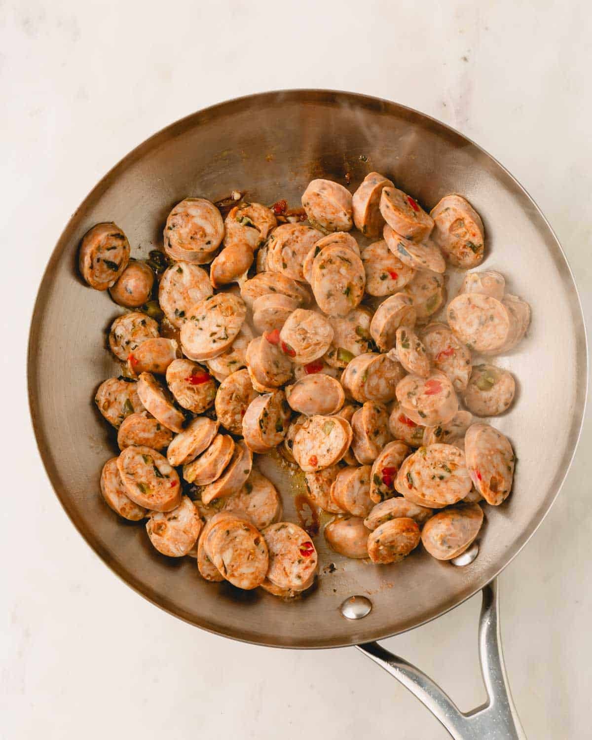 A skillet with Italian chicken sausage rounds cooking.