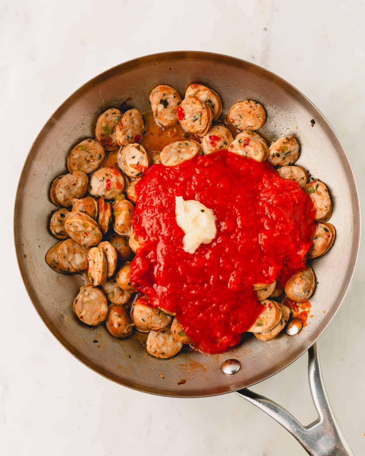 A skillet with Italian chicken sausage rounds, marinara sauce, and butter.