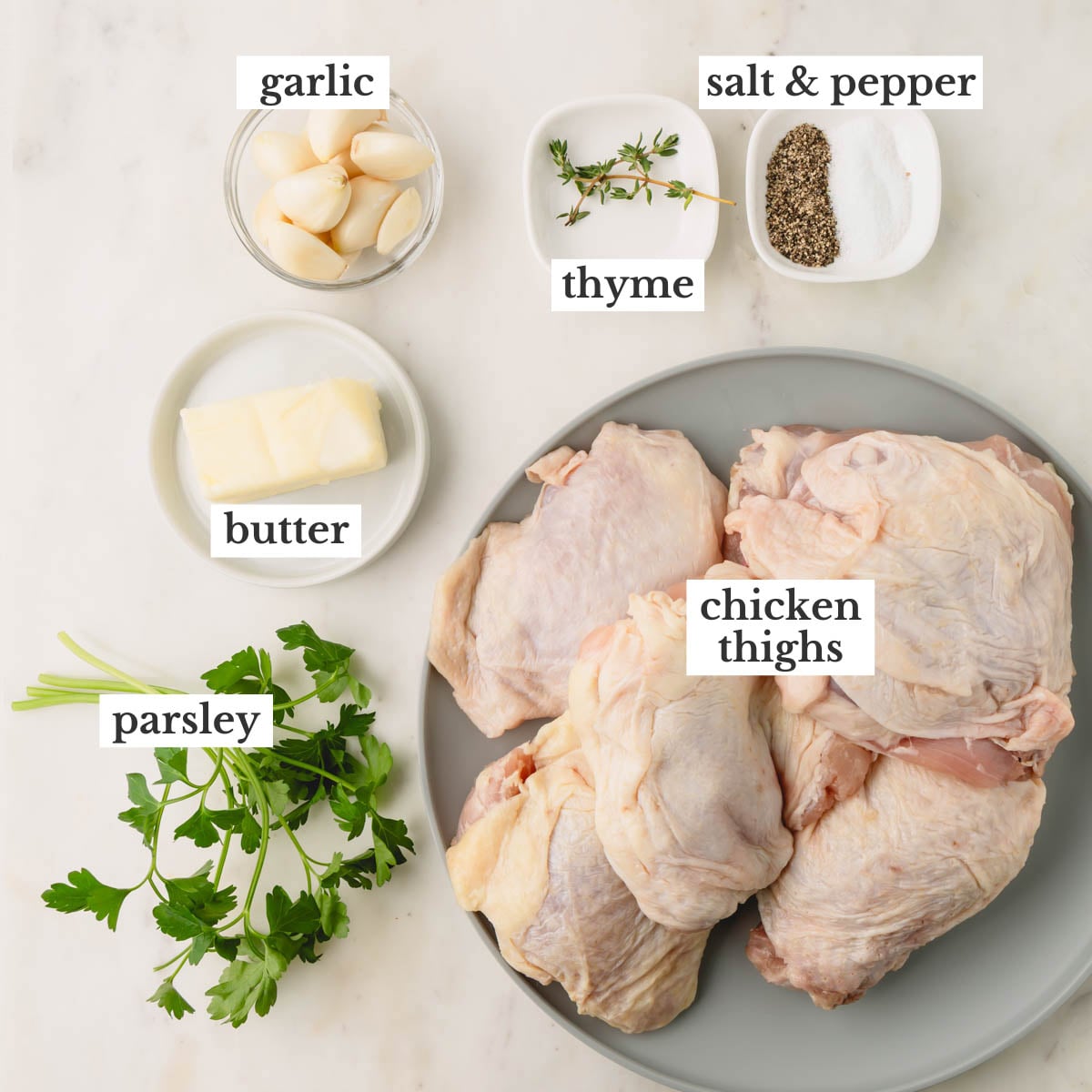 Ingredients for garlic butter chicken thighs which include garlic cloves, butter, parsley, thyme, chicken thighs, salt, and pepper.