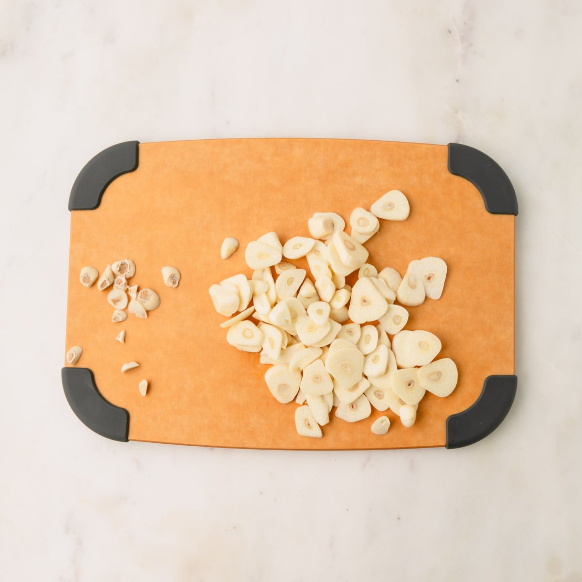 Sliced garlic cloves on a brown cutting board.