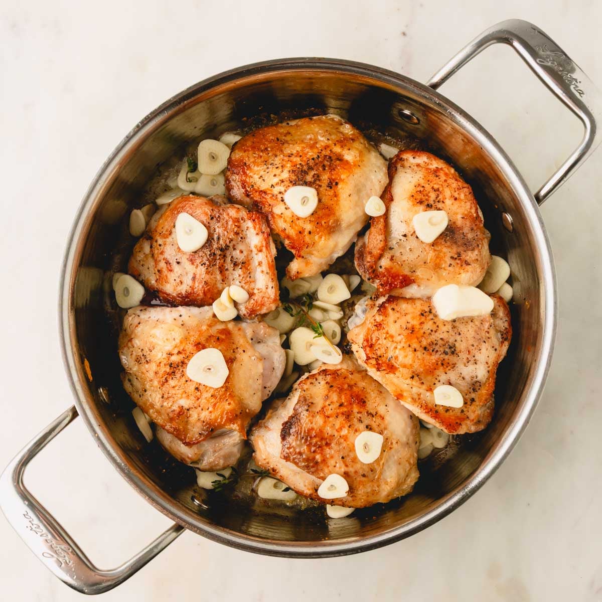Chicken thighs are skin-side up in the skillet and thinly sliced garlic cloves are added.