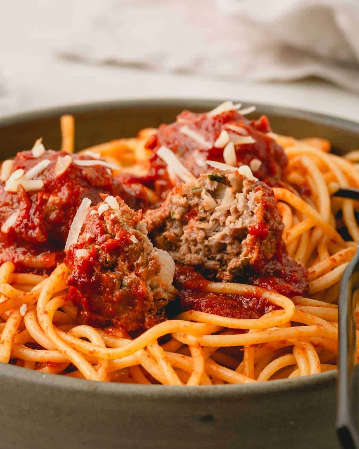 A close up image of a meatball without breadcrumbs in tomato sauce on top of pasta.