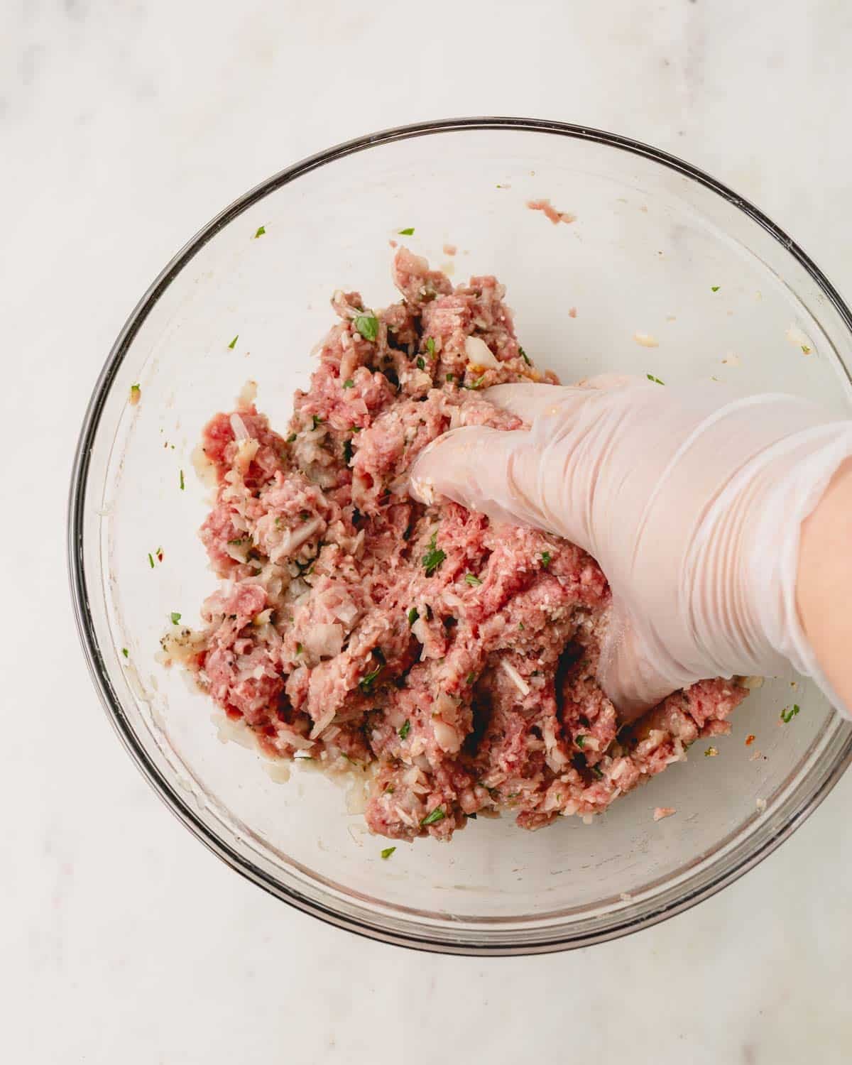 A hand with a glove is mixing the ground beef meatball mixture.