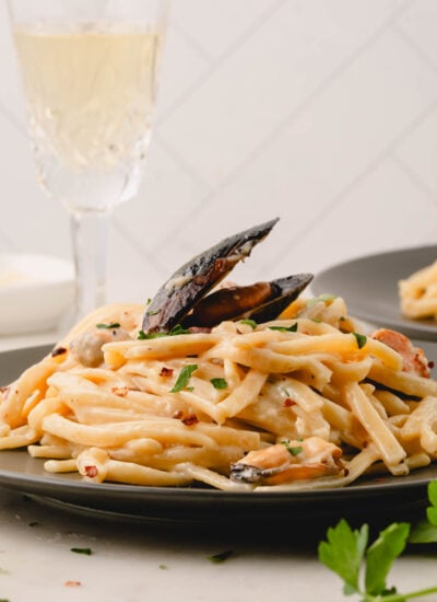 Pasta with mussels on a black plate with a glass of wine.