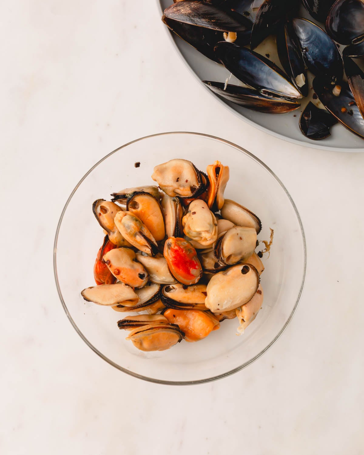 The cooked mussels are removed from their shells into a glass bowl.
