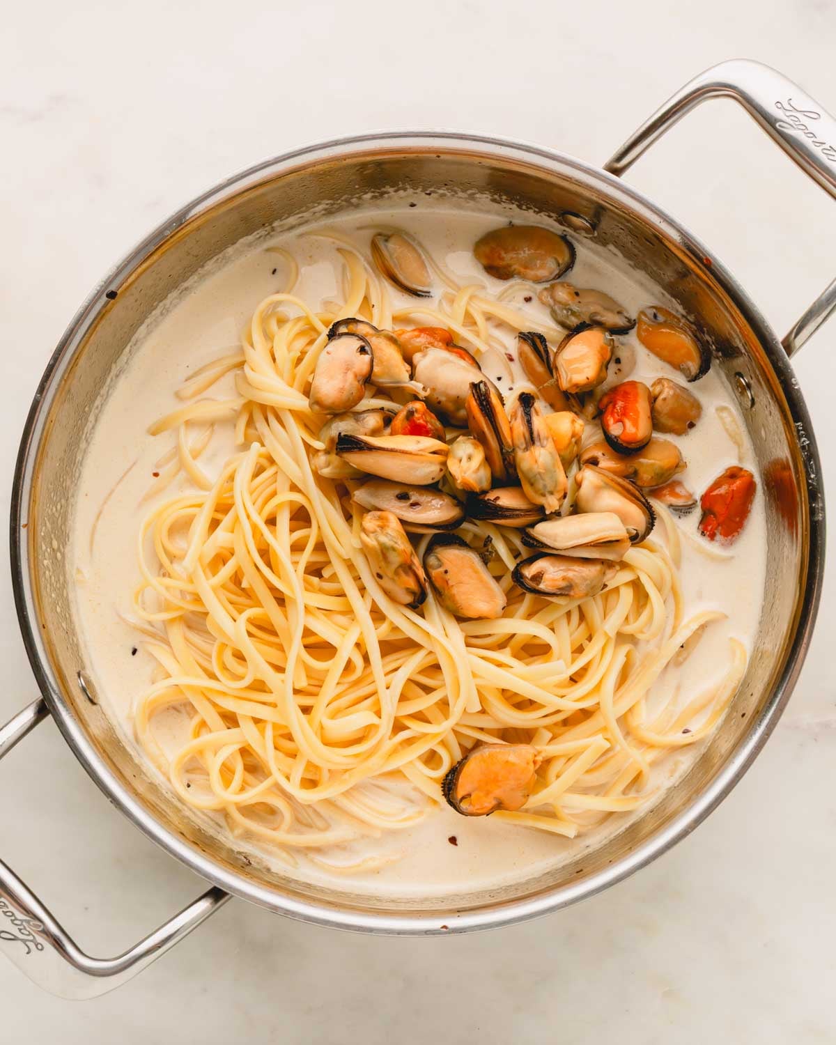 Linguine and cooked mussels are added to the white wine cream sauce in the skillet.