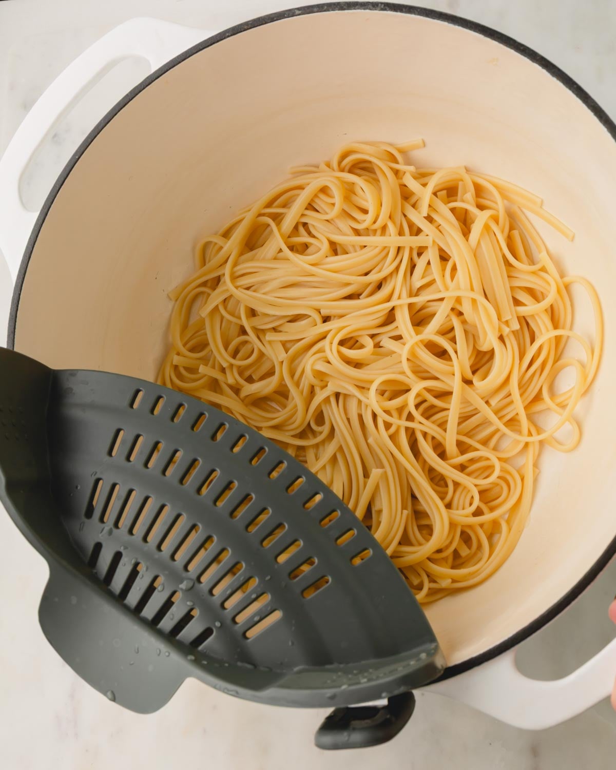 Boiled linguine noodles being drained from a large pot.