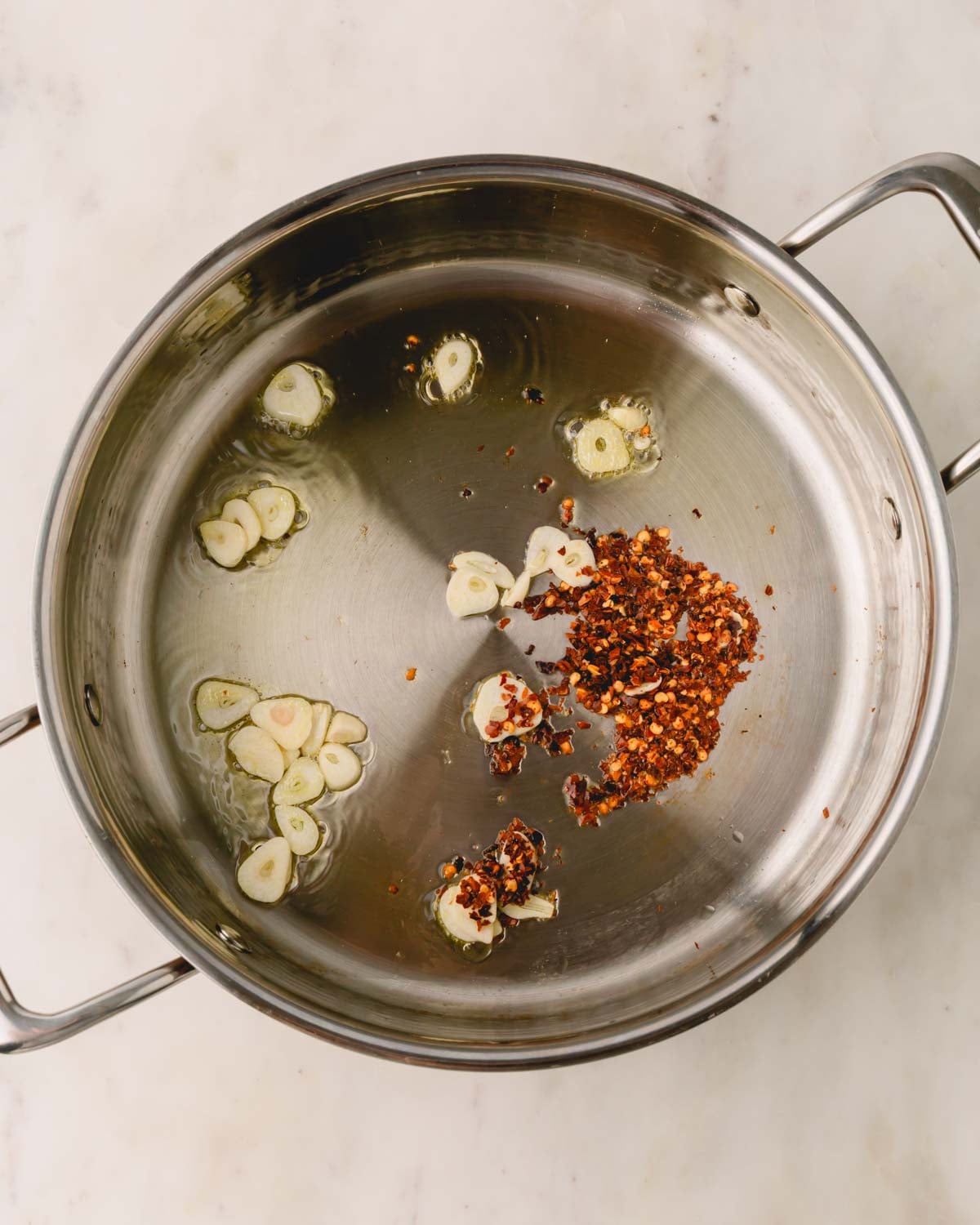 A saute pan with garlic and chili flakes cooking in olive oil.