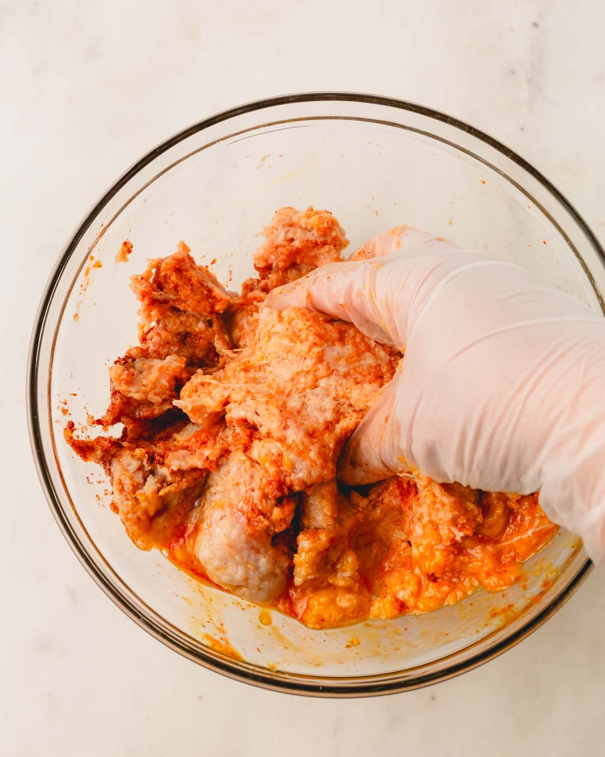 A hand is mixing the ingredients for the chicken burger mixture in a bowl.