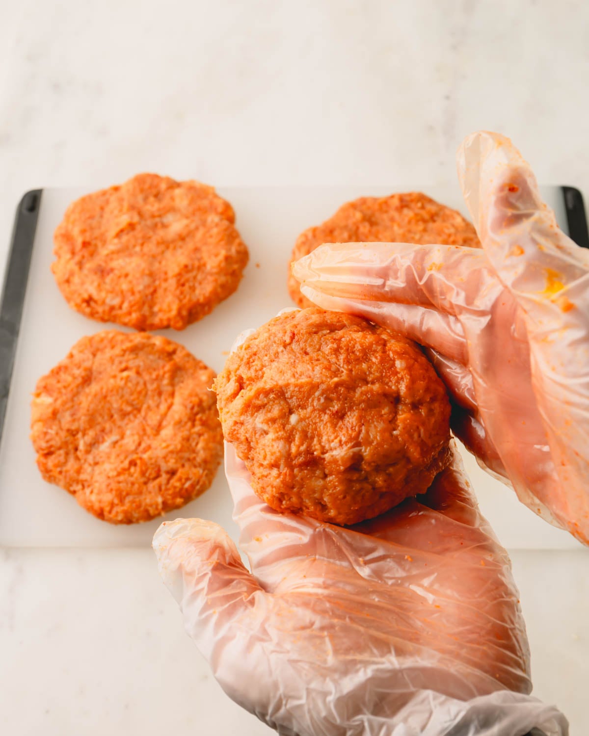 Two hands with gloves shaping the spicy chicken burger patties.