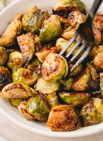 Balsamic honey Brussels sprouts in a white bowl with a black fork.