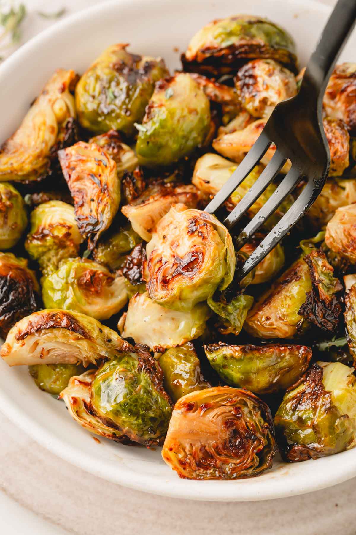 Balsamic honey Brussels sprouts in a white bowl with a black fork.