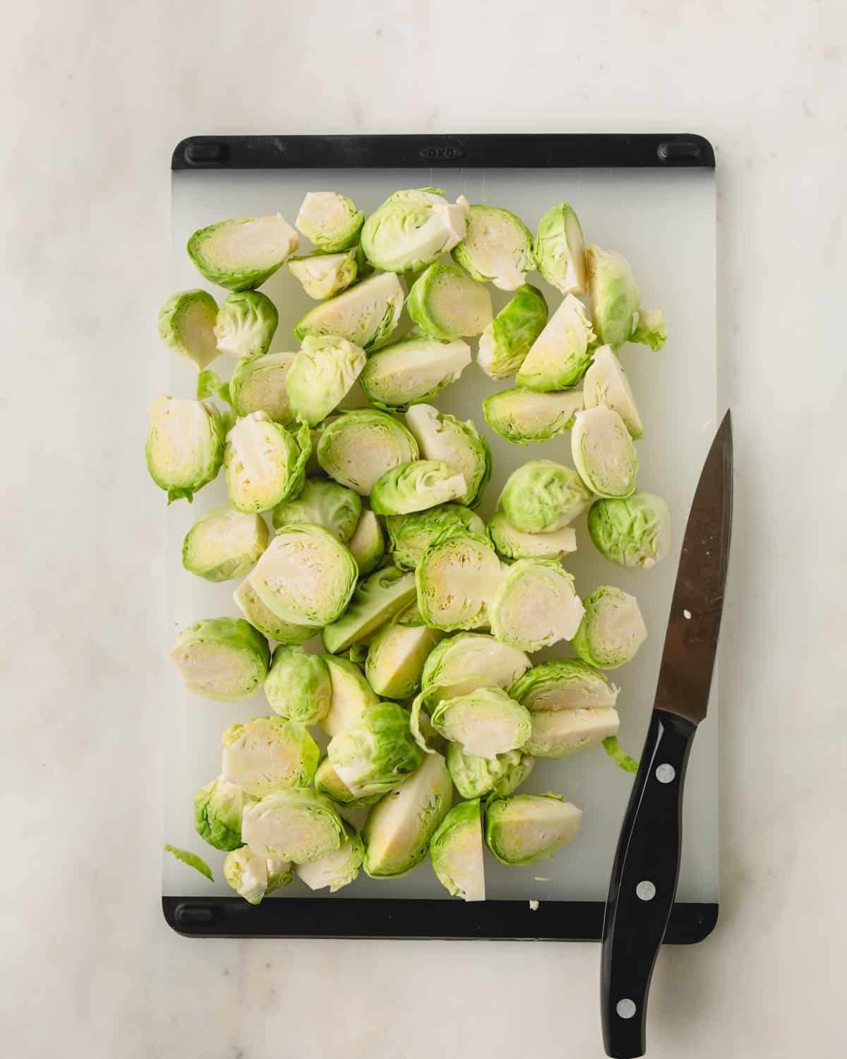 A knife cutting Brussels sprouts in half on a cutting board.