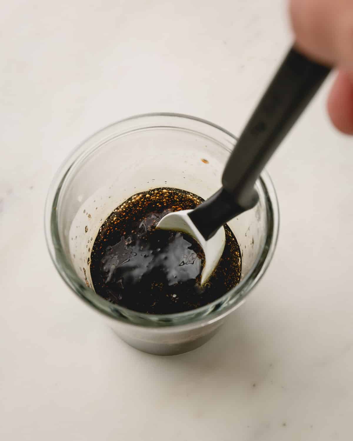 A glass bowl with honey and balsamic vinegar in it. A hand is stirring with a spoon.